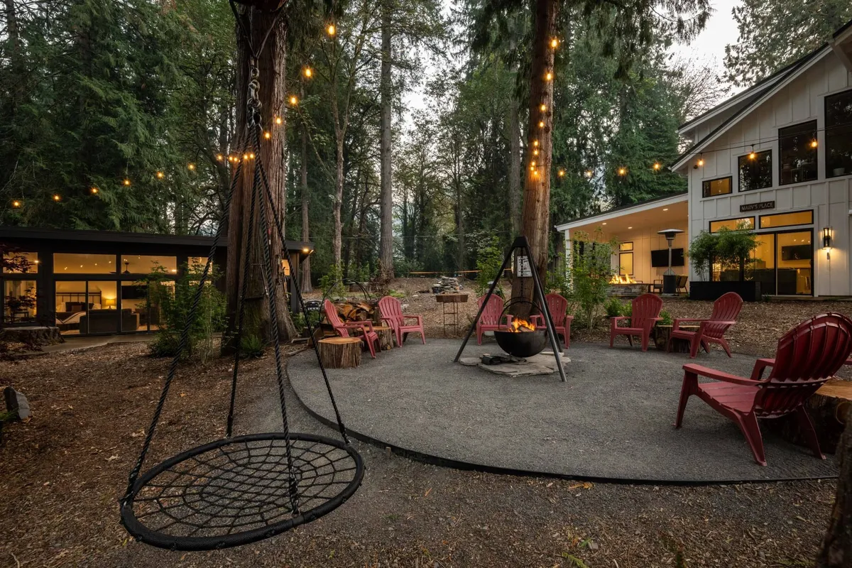 An inviting outdoor gathering space with a swing chair, fire pit, red Adirondack chairs, and glowing string lights under the night sky. The setting encourages communal gatherings, storytelling, and relaxing after a day of exploration.