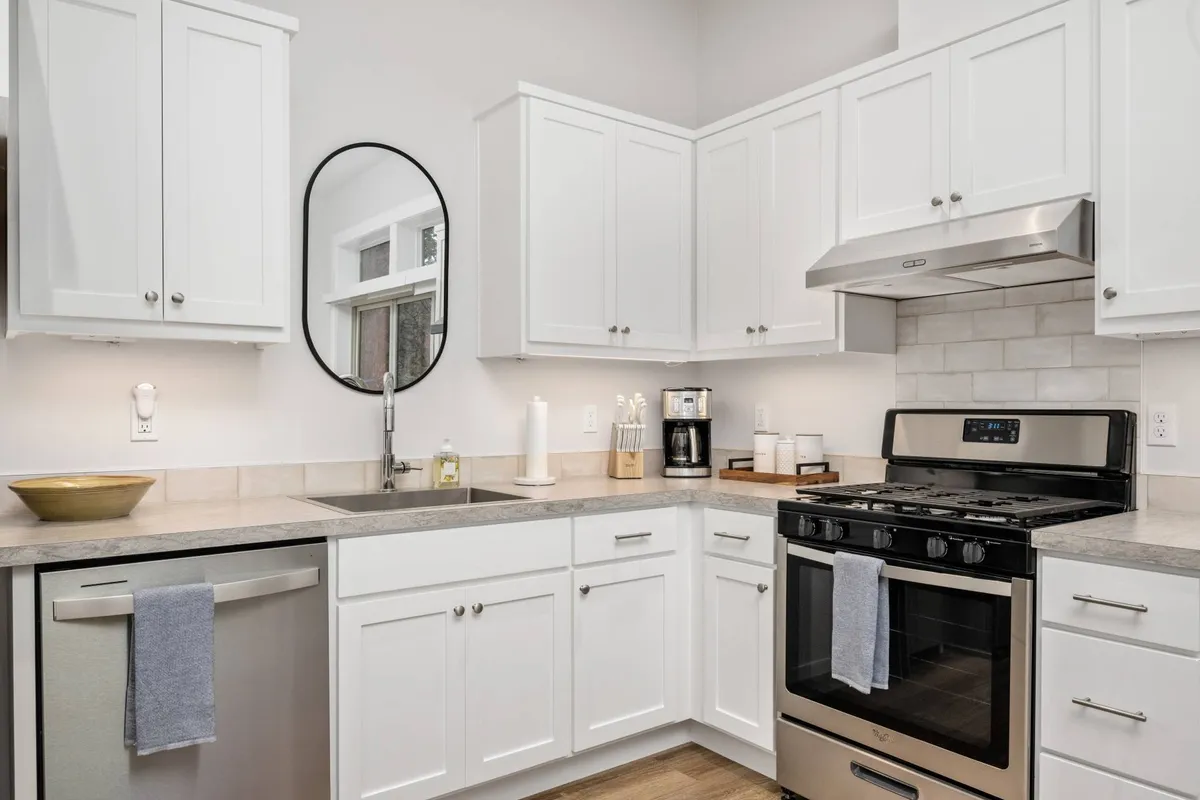 A bright, modern kitchen area featuring stainless steel appliances, white cabinetry, a central kitchen island, and a large mirror, all set within a welcoming space ideal for cooking or entertaining.