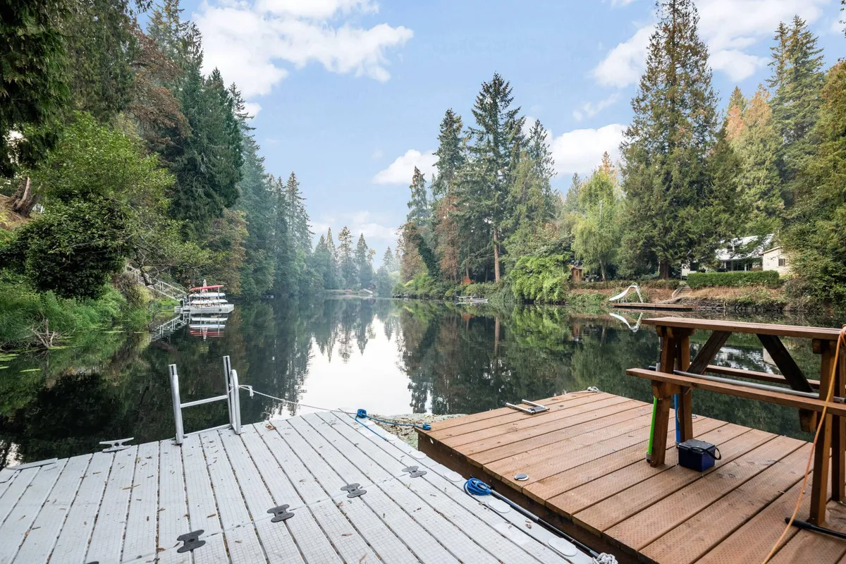 A scenic exterior image showing a wooden dock extending over a calm body of water, surrounded by trees with boats moored nearby. The setting sun casts a warm glow, adding to the peaceful mood.