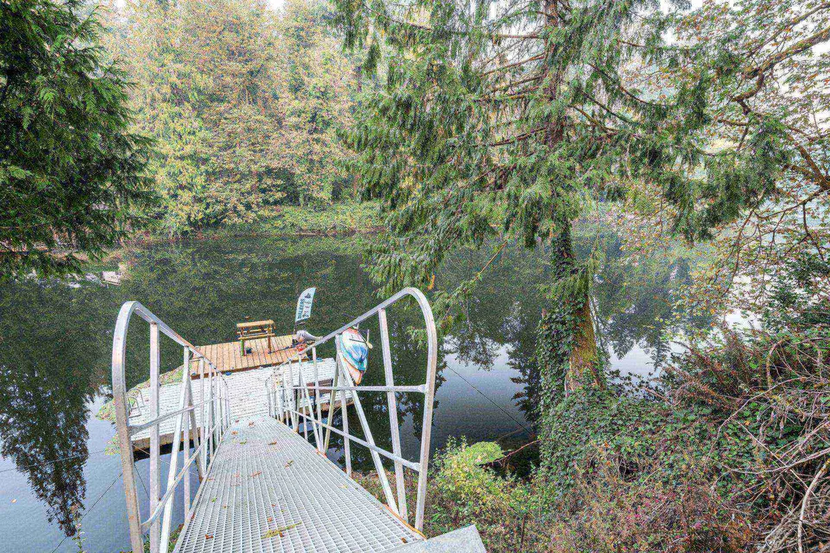 A serene metal dock extends over calm water, bordered by tranquil trees and offering a simple seating area. The peaceful setting is ideal for relaxing, enjoying views, fishing, or launching a kayak, encapsulating river access and the tranquil ambiance described.