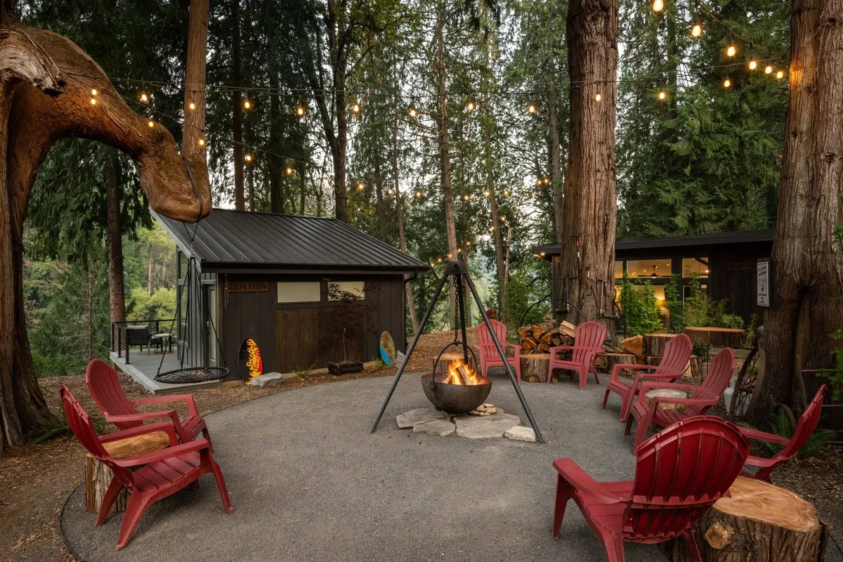 A warmly lit fire pit circled by red chairs and twinkling string lights set against a backdrop of leafy trees. The ambiance is inviting and communal, ideal for stargazing, storytelling, or simply unwinding with neighbors.