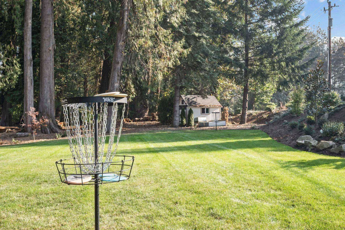 A lush green lawn with a disc golf basket, surrounded by trees and a small shed in the background. The open area is ideal for recreation, picnics, or letting pets explore (while leashed), reinforcing the outdoor adventure theme.
